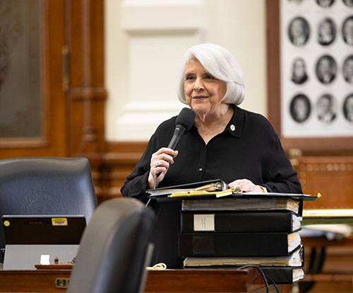 Photo: Dean Senator Judith Zaffirini holding the microphone at her desk in the Chamber